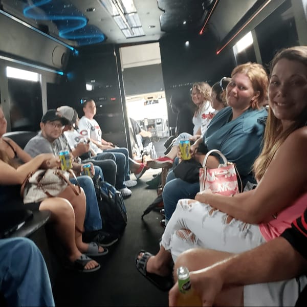 People sitting inside a party bus with blue neon lights, some holding drinks.