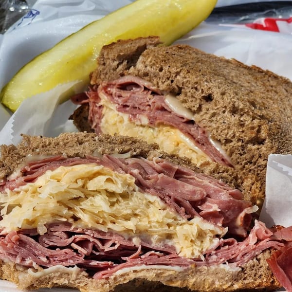 A close-up of a Catanzaro's Reuben sandwich with corned beef, sauerkraut, and a pickle spear.