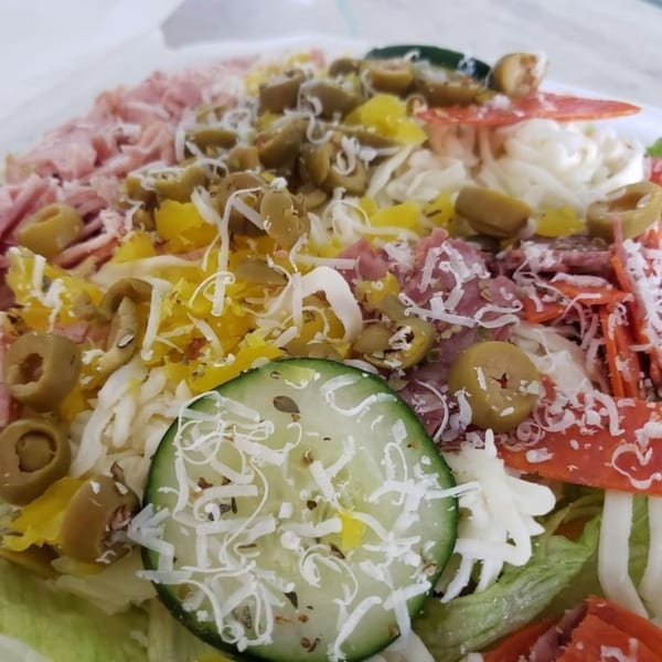 Close-up of a vibrant antipasto salad with ham, pepperoni, olives, cheese, and a cucumber slice.